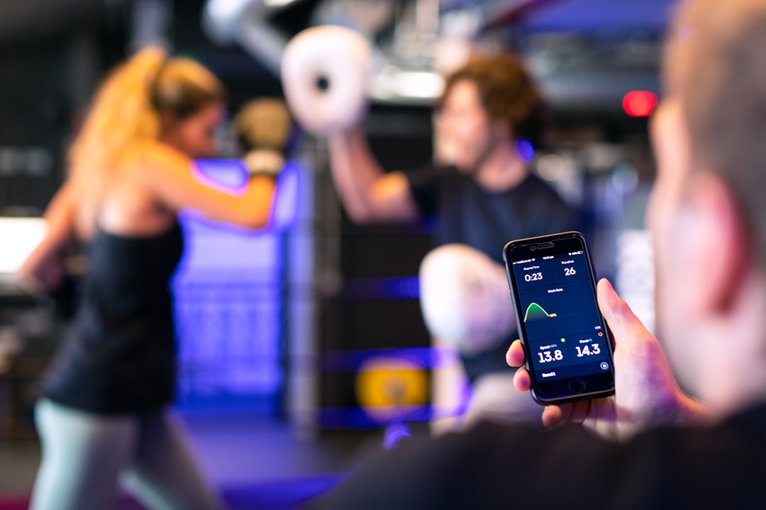 Male engineer monitors boxing performance through athletic devices. Female boxer and trainer train in background.